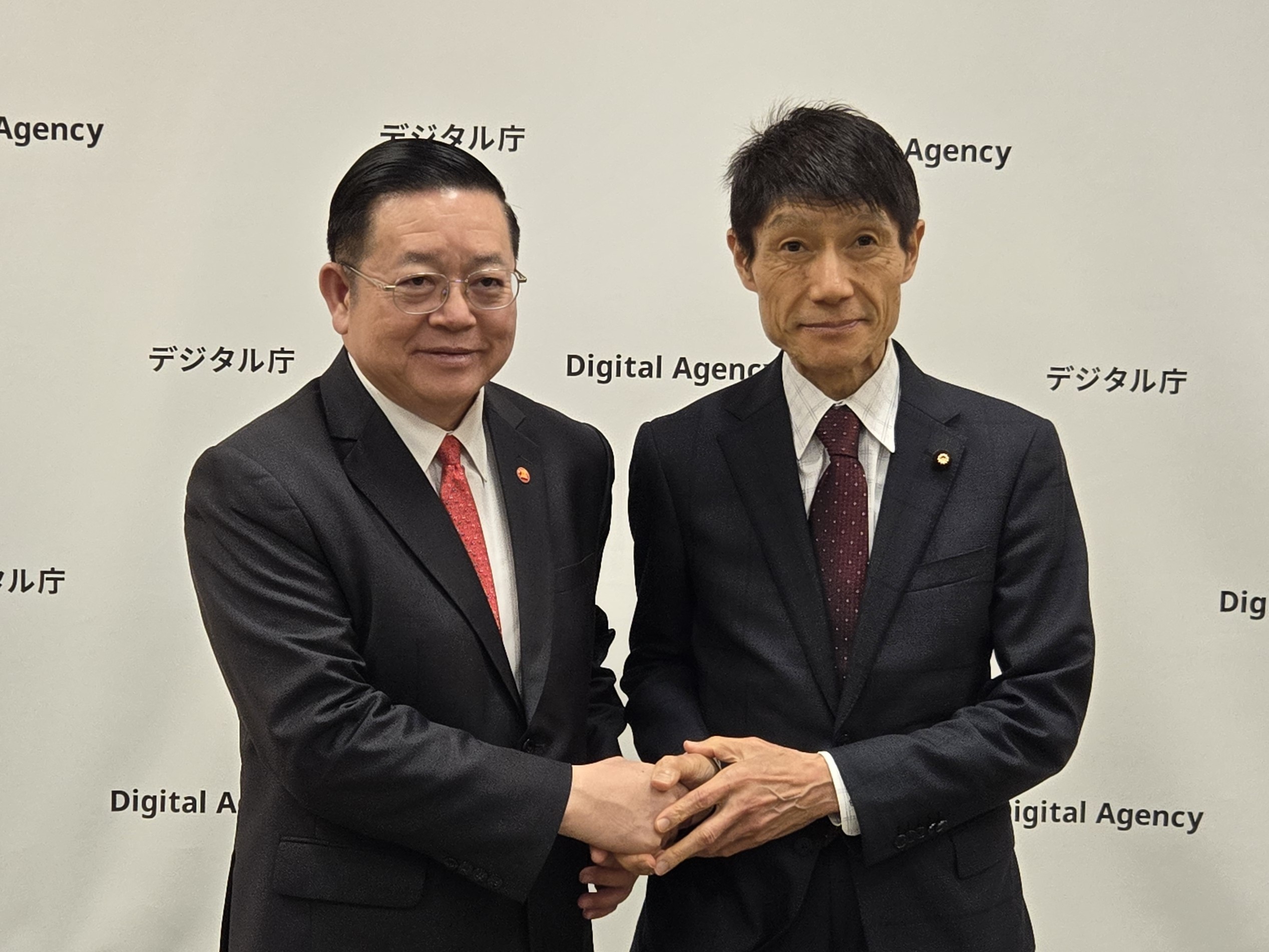 カオASEAN事務総長（左）と古川デジタル大臣（右）とデジタル庁のロゴパネルの前で握手を交わす様子。