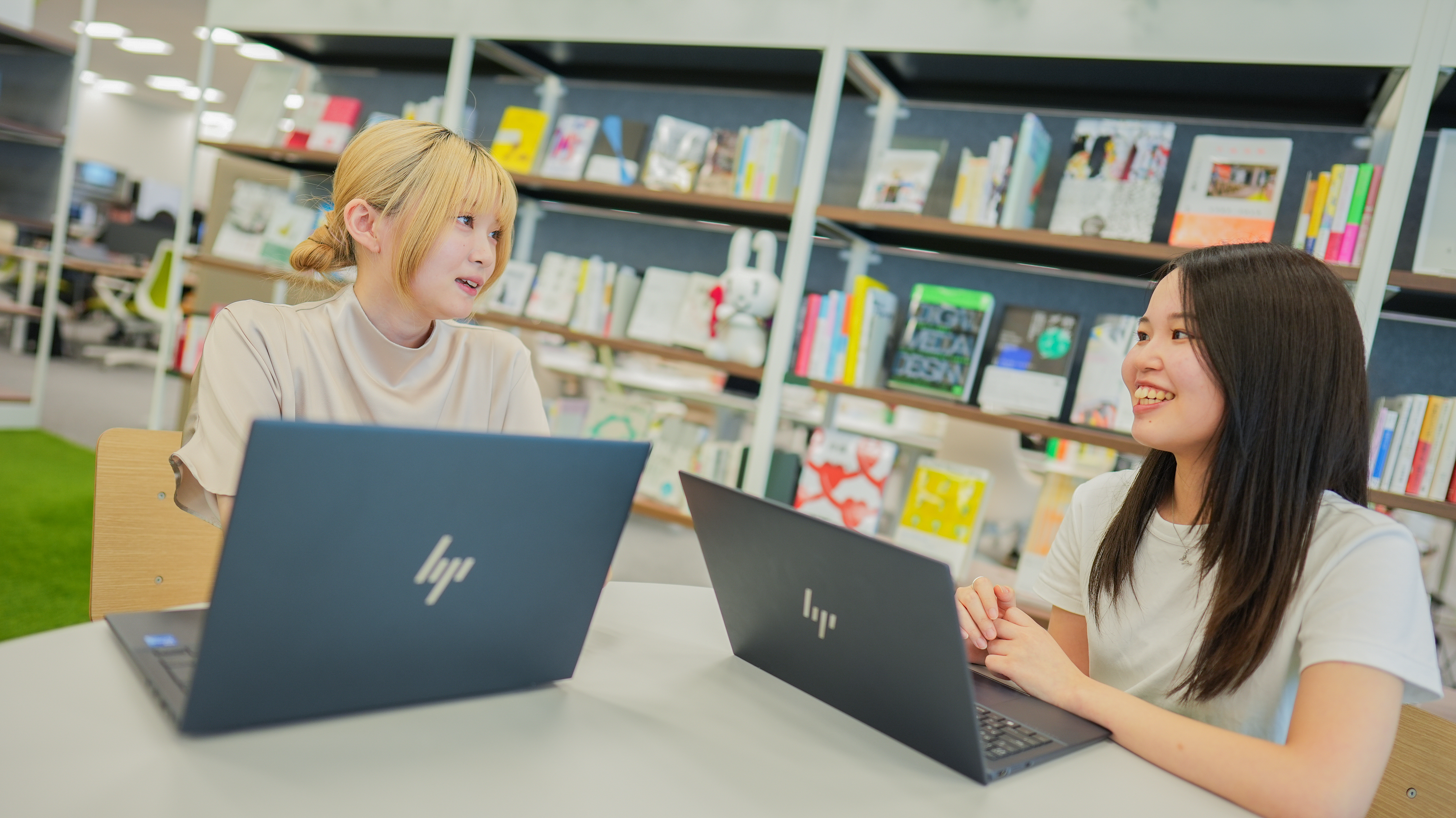 A picture of two people talking on a laptop&comma; with a bookshelf in the background and a row of books&period; 