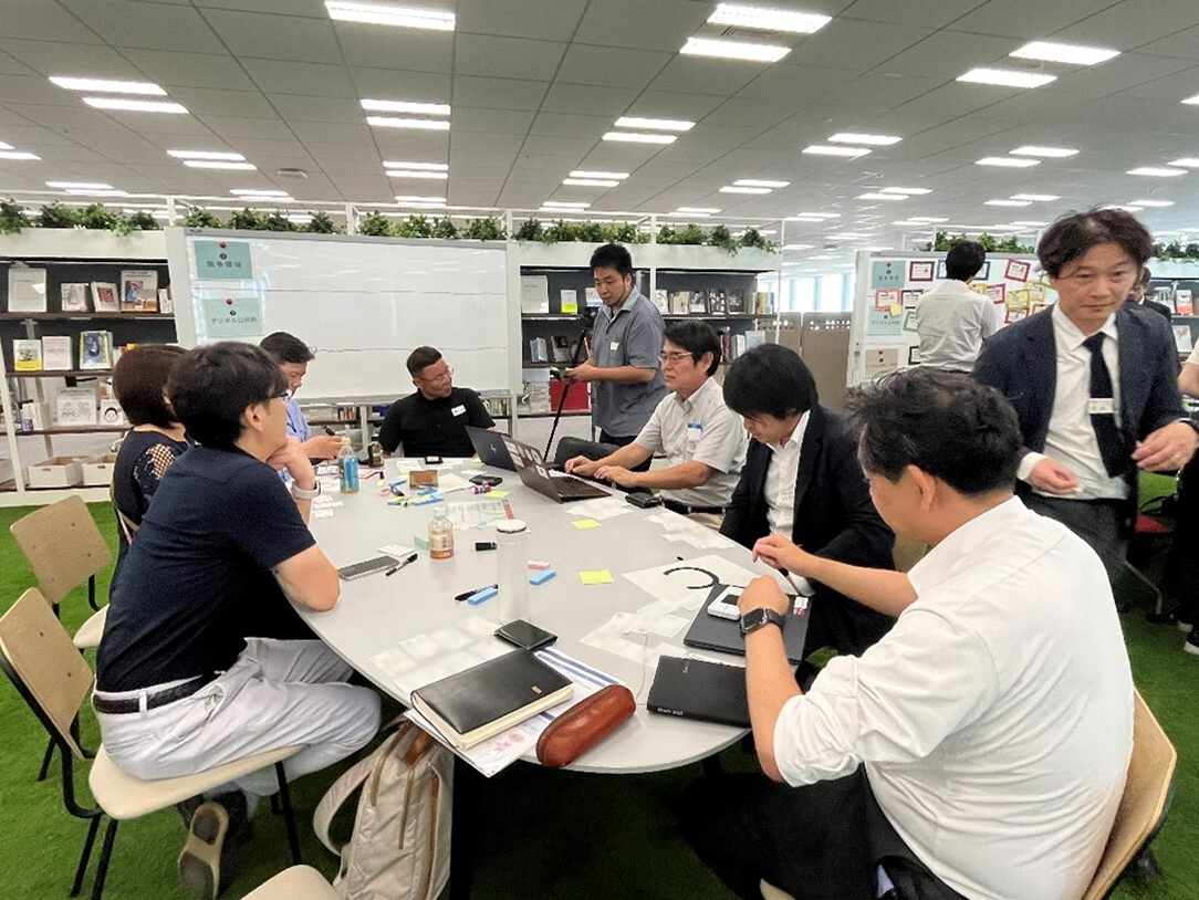 Photo of six participants sitting face-to-face in a round table and having a discussion using a computer or a label paper