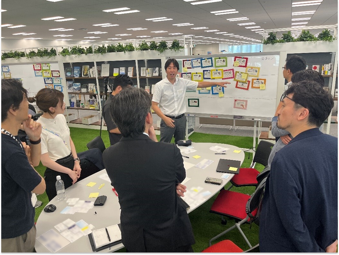 A whiteboard is in the middle with a man standing next to it, talking to four participants in the photo