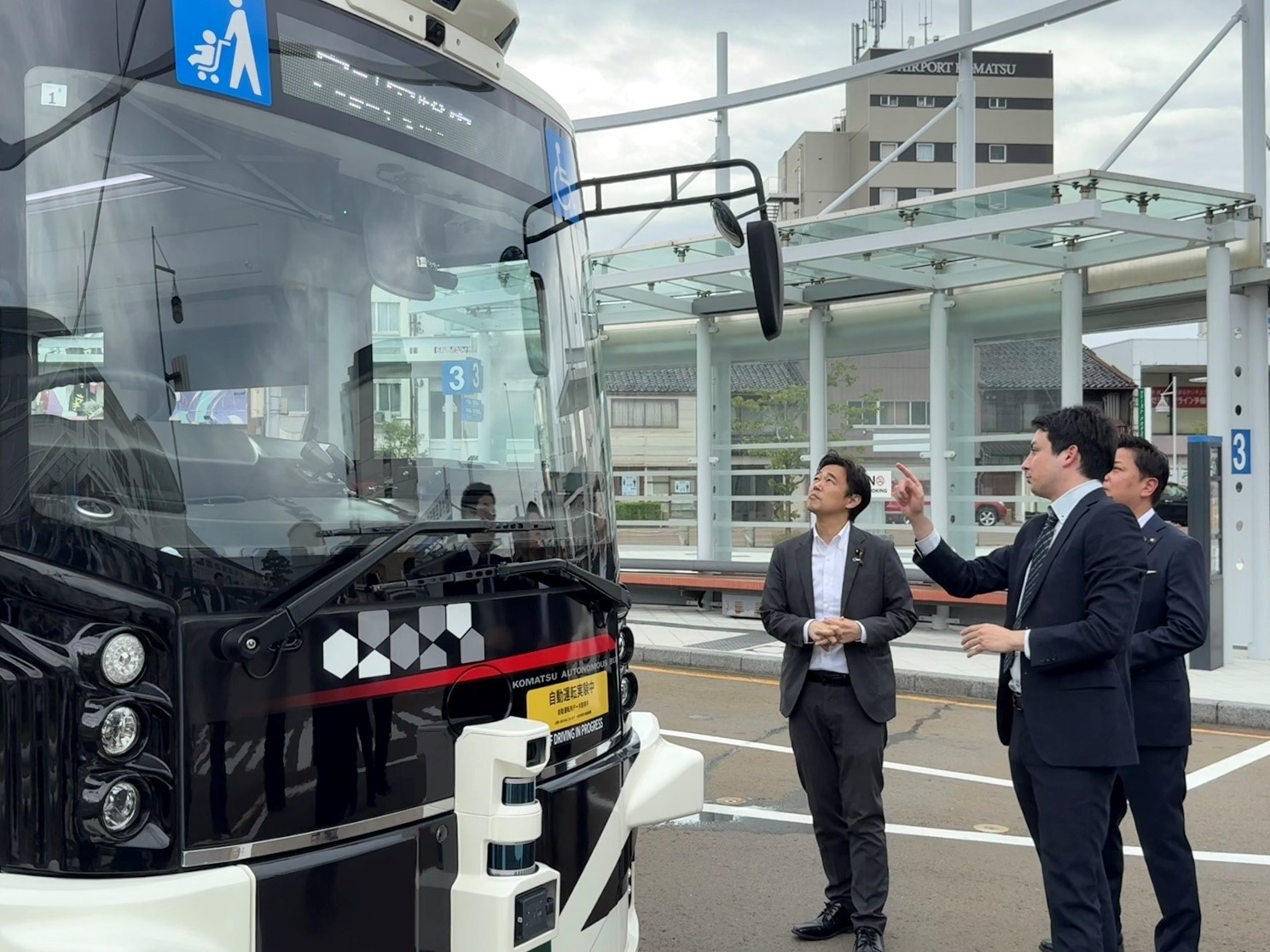 自動運転バスの外からバスの説明を受けている。穂坂副大臣は見上げながらバスを見ている写真。