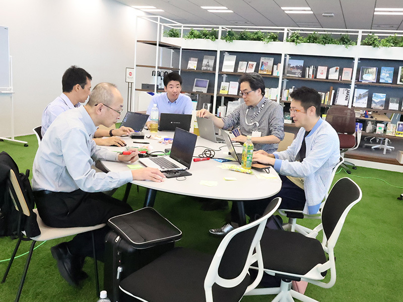 A picture of five people sitting around a table looking at a computer screen. 