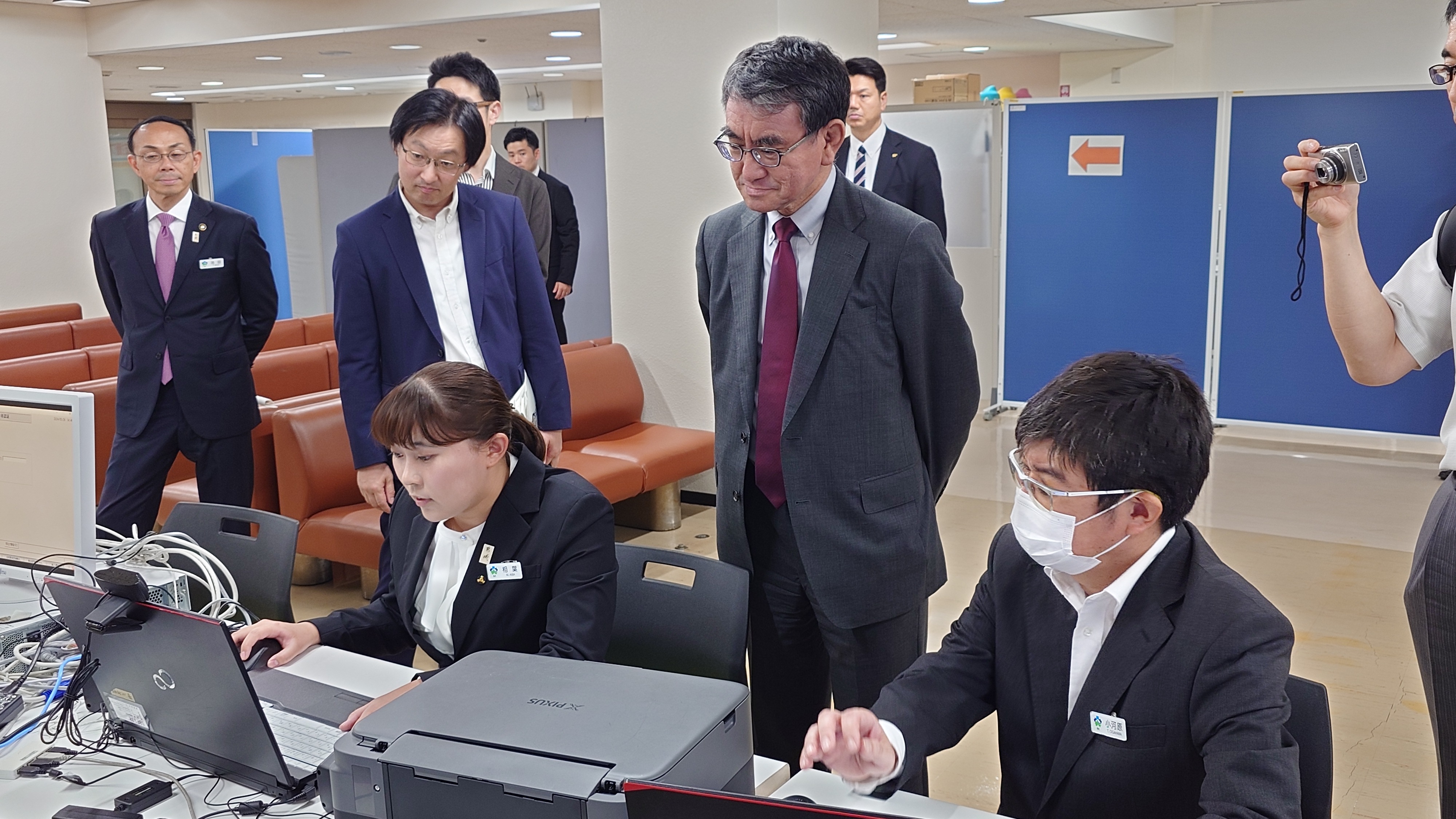 In the picture, Minister for Digital Transformation Kono inspects the operation of identity verification in cooperation with the staff of the post office to which the Issue application administration of My Number Card is entrusted.