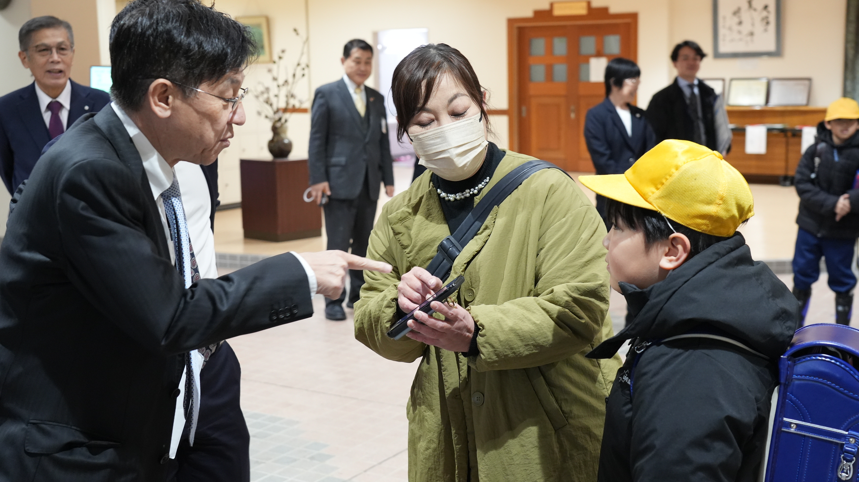 松本デジタル大臣がスマートフォンを指さしながら、親子からみまもり通知について説明を受けている様子。