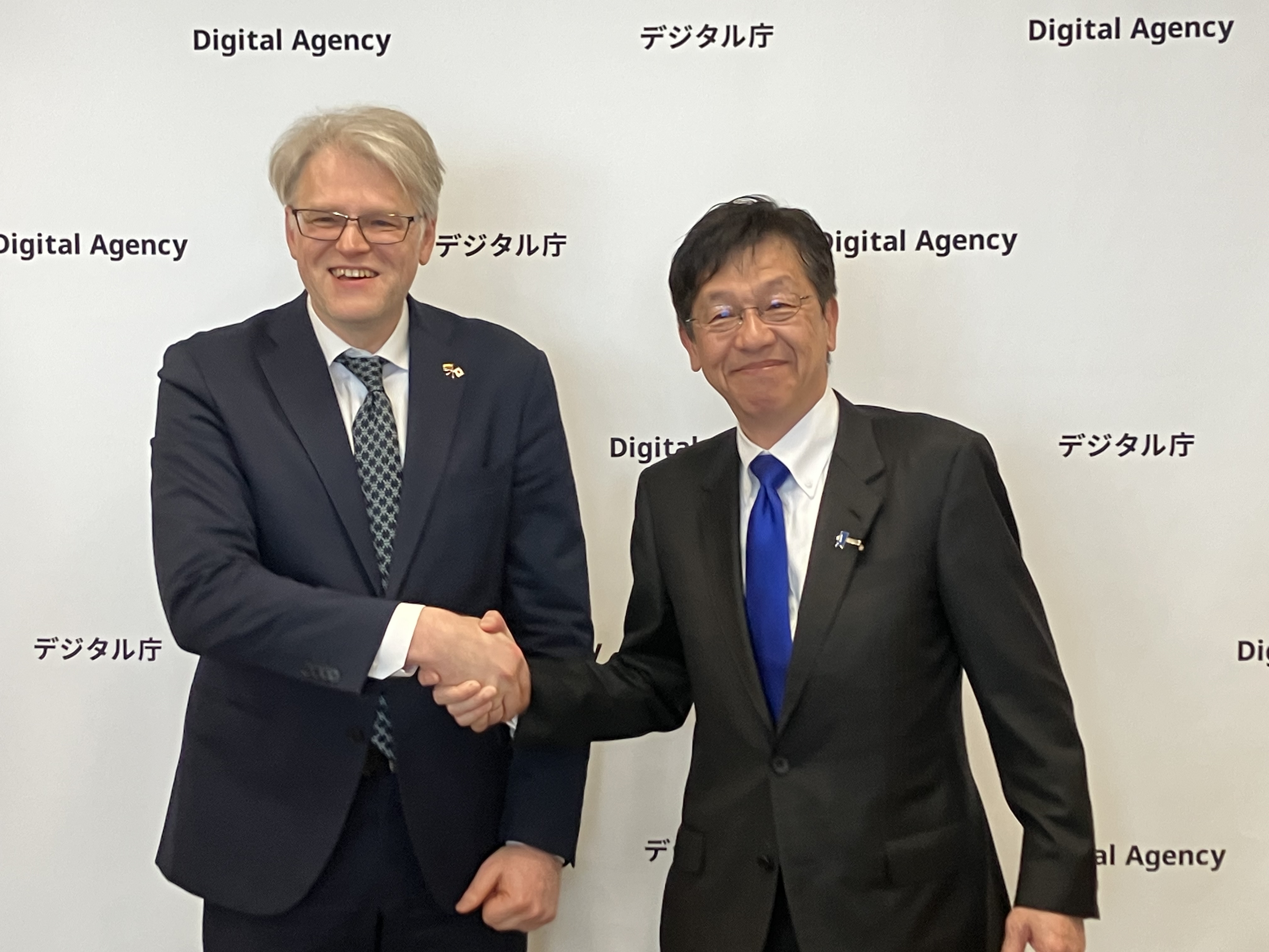 Dr. Aurelijus Zykas, Ambassador of the Republic of Lithuania to Japan (left) and Minister for Digital Transformation Matsumoto (right) shake hands in front of a backdrop featuring the Digital Agency logo displayed repeatedly.