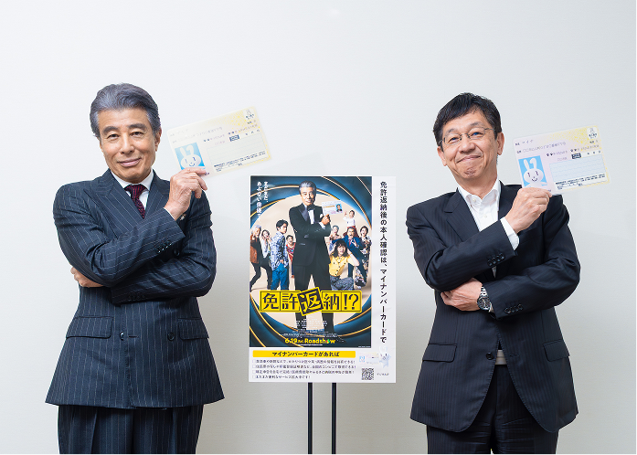 Minister for Digital Transformation Matsumoto and the lead actor Hiroshi Tachi stand side by side in suits, smiling with their arms crossed. Each holds a My Number Card above their left shoulder, copying Hiroshi Tachi's pose from the "Goodbye My Car" poster shown in the center.
