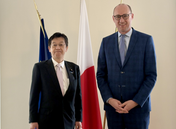 Minister for Digital Transformation Matsumoto (left) and Deputy Prime Minister Vincent Van Peteghem (right) standing side by side in front of the flags of Japan and Belgium, facing forward.
