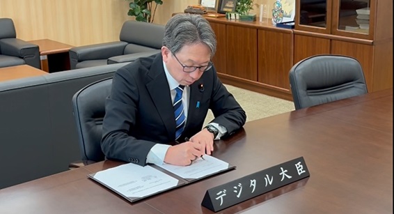 Digital Minister Taira, seated, signing the Memorandum of Cooperation with the Kingdom of Bahrain. The nameplate “Digital Minister” in Japanese displayed in front of him.