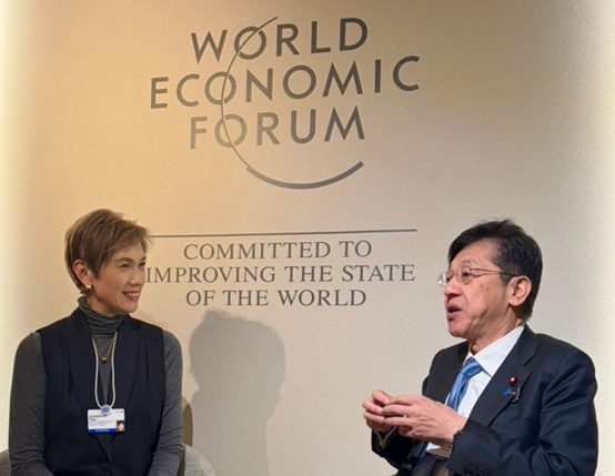 Minister Matsumoto (right) discussing with Mrs. Josephine Teo, Minister for Digital Development and Information of Singapore (left), with the WEF logo panel in the background.