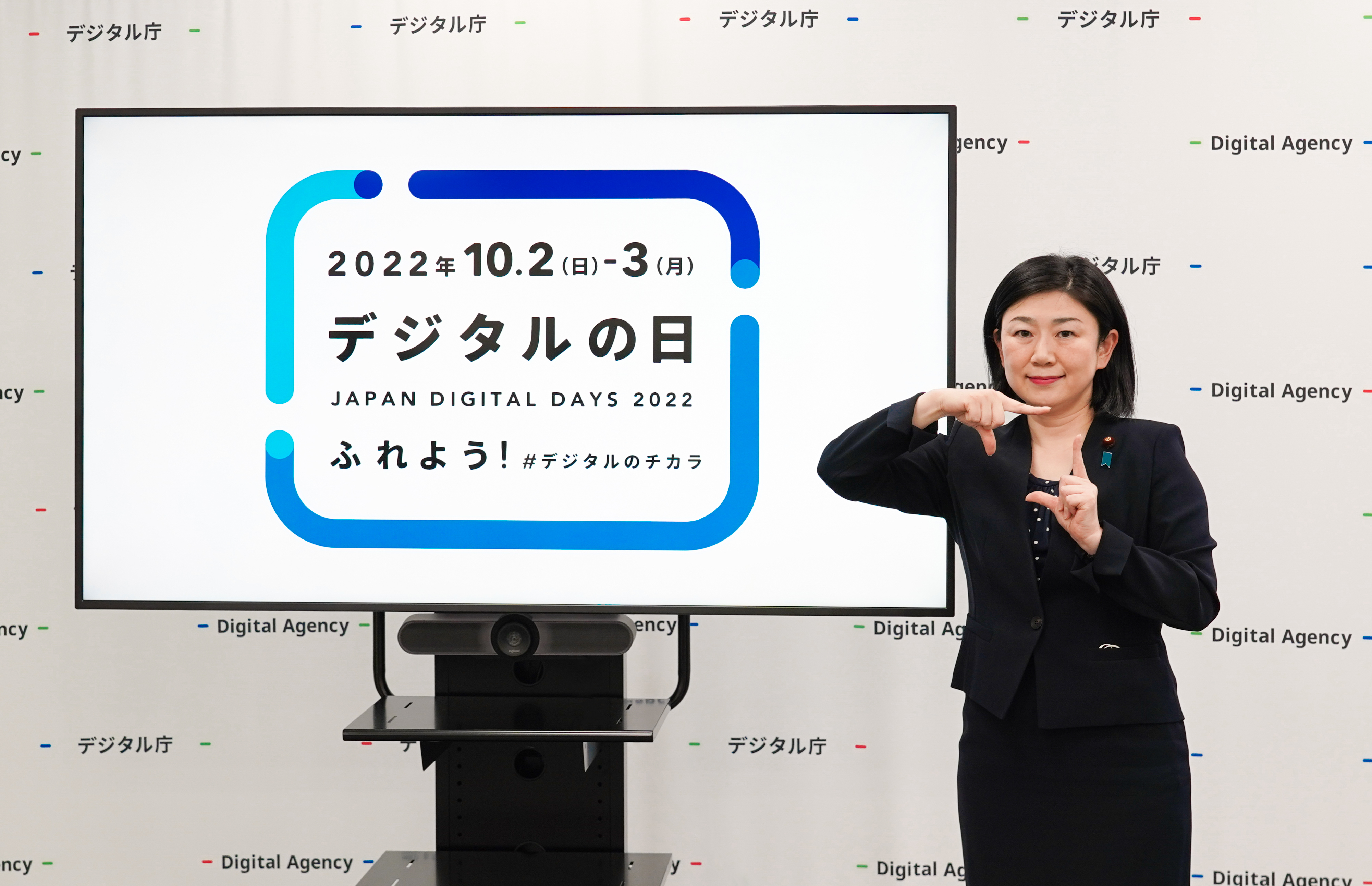 The 2022 Digital Day logo image is displayed on a monitor, and MAKISHIMA Karen Minister for Digital Transformation stands to the right of the monitor with a hand sign of the logo.