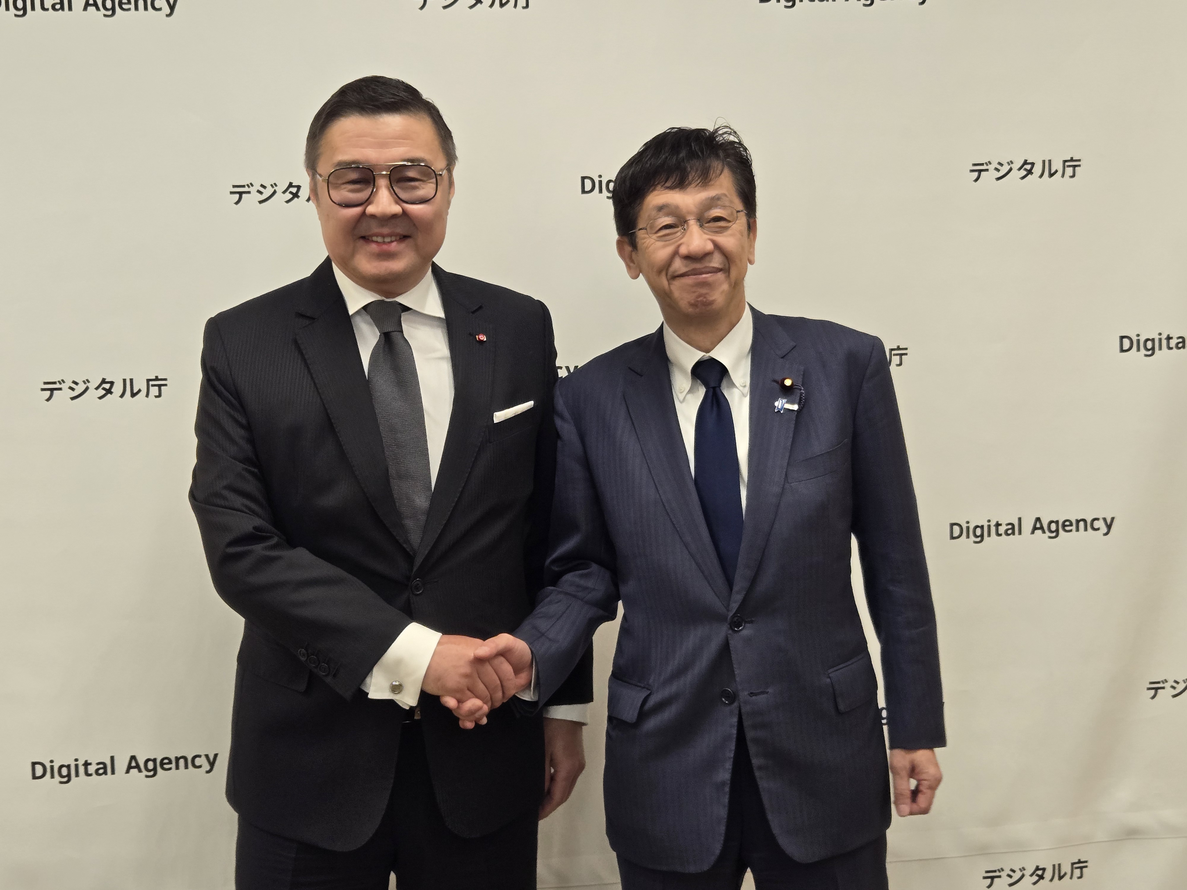 左にイェルラン・バウダルベック・コジャタエフ駐日カザフスタン共和国特命全権大使、右に松本デジタル大臣。2人が笑顔で握手を交わしている。