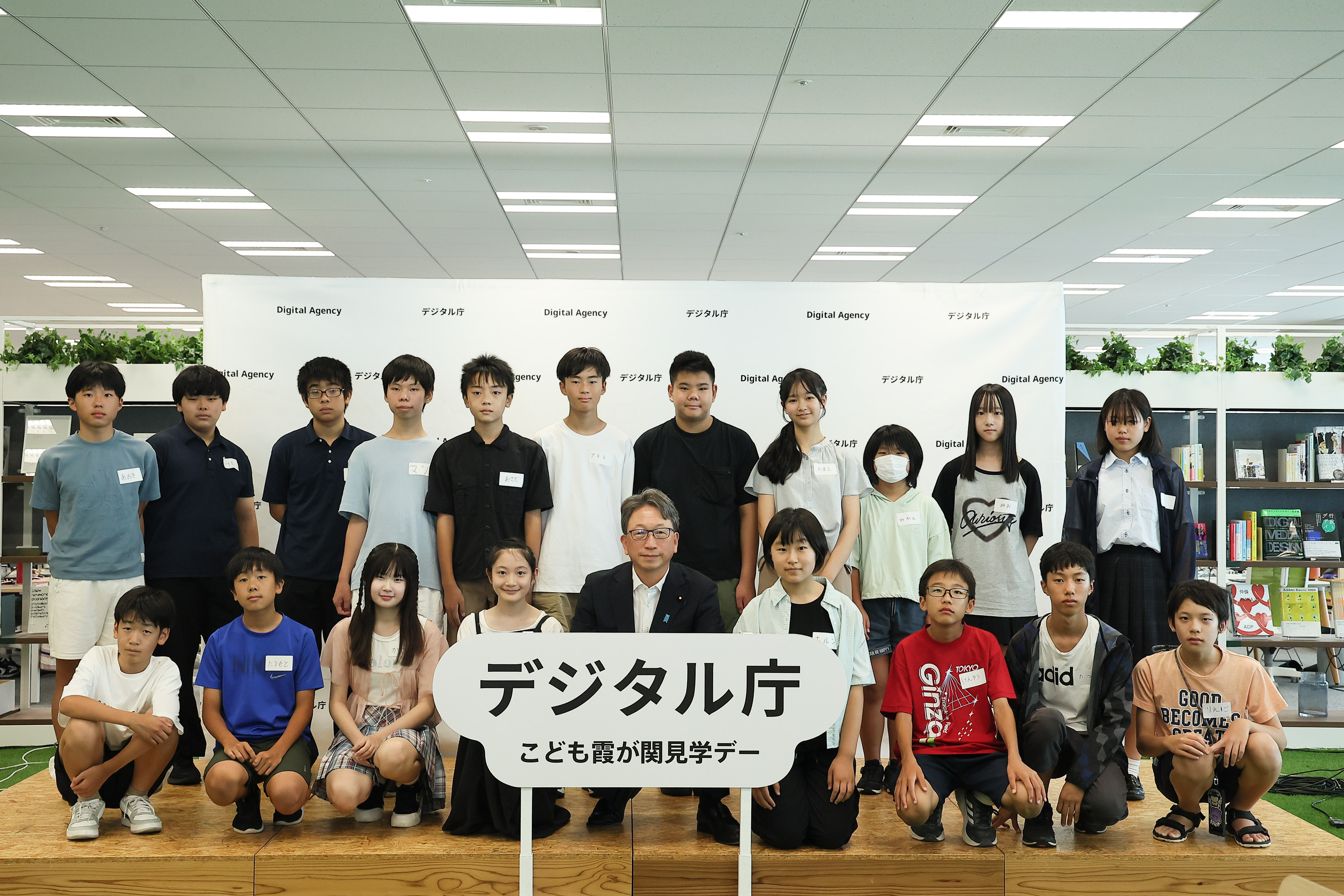 On the stage, which is decorated with a panel with the logo of "Digital Agency Children's Kasumigaseki Tour Day," junior high school students who participated in the workshop and Mr. Taira, Minister for Digital Transformation are standing in two rows. The front row is squatting and the back row is standing.